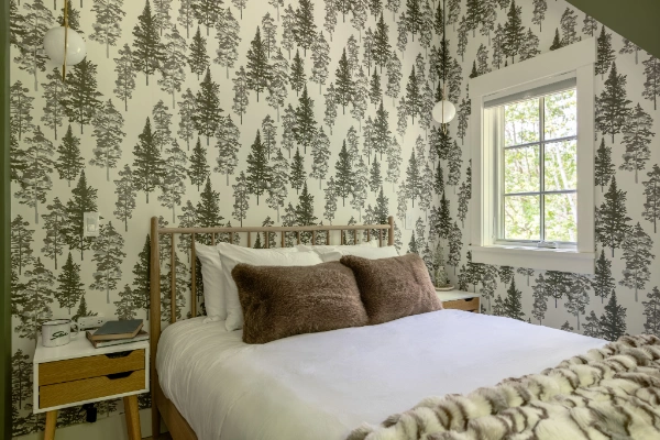 Bedroom with forest-pattern wallpaper, wood bed frame, soft neutral bedding, and window overlooking trees